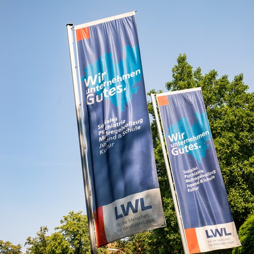 Zwei Flaggen mit LWL-Logo wehen im Wind.