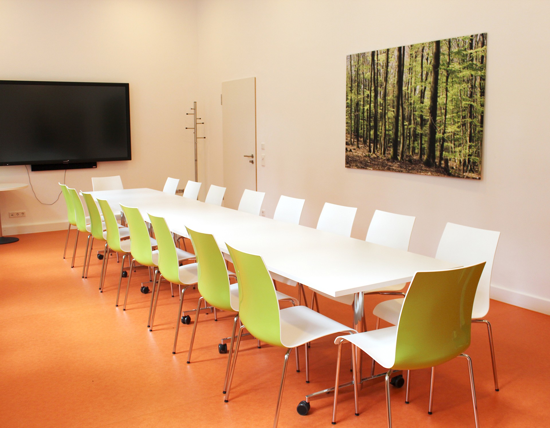 Ein Konferenzraum der Sucht-Reha mit einem großen Tisch, vielen Stühlen und einem großen Fernseher an der Wand